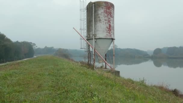 Bir sonbahar sabahı yansıtıcı bir göle bakan bir eski metal silo dron atış — Stok video