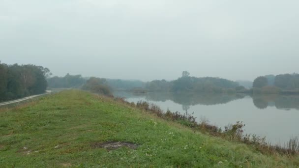 Pan się strzał drone metalowe silosu na trawiastą wzgórzu z widokiem na jezioro jasne odblaskowe na mglisty jesienny poranek — Wideo stockowe