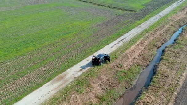 Roterende luchtfoto van een man die naast een auto op een lege landelijke weg in de landerijen van Cresnjevec, Slovenië — Stockvideo