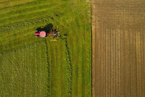 Luftaufnahme eines roten Traktors, der Ackerland mit einem Spinngestell bewirtschaftet — Stockfoto