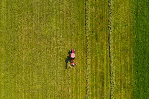 Vista aerea dall'alto verso il basso di un trattore rosso che coltiva terreni agricoli con uno spinning rack — Foto Stock