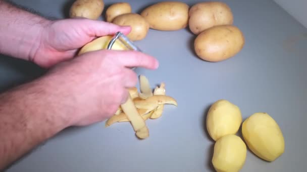 Mans hands peeling potatoes with kitchen peeler — Stock Video