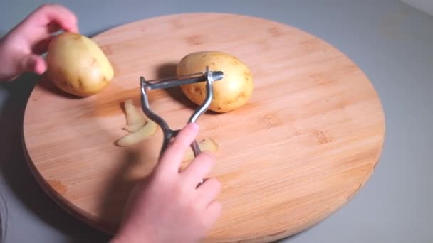 Handen van klein meisje peeling aardappelen met dunschiller op houten bureau — Stockvideo