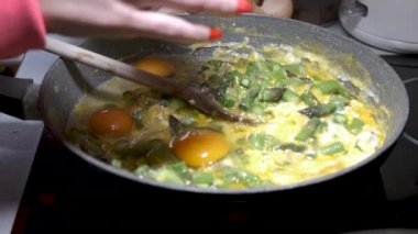 Soğan ve yumurta ile yeşil kuşkonmaz, bir tavada karıştırarak kadın