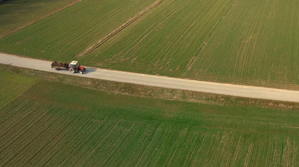 Veduta aerea di un trattore rosso e di un rimorchio che trasportano un carico di letame su strada — Foto Stock