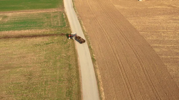 Veduta aerea di un trattore rosso e di un rimorchio che trasportano un carico di letame su strada — Foto Stock