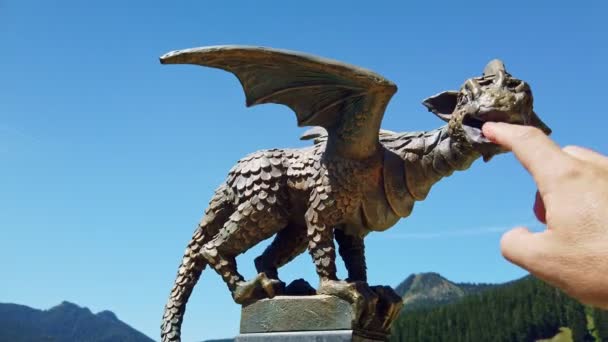 Dedo masculino provocando um dragão, estátua de dragão de bronze no pólo, paisagem montesa, floresta e pasto alpino — Vídeo de Stock