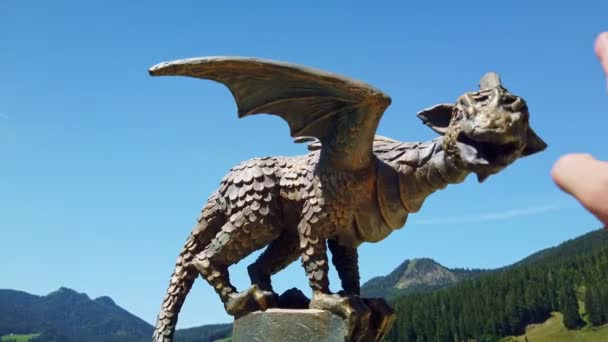 Bronze dragon statue on pole, mountain landscape, forest and alpine pasture, male hand touching and caressing the dragon — Stock Video