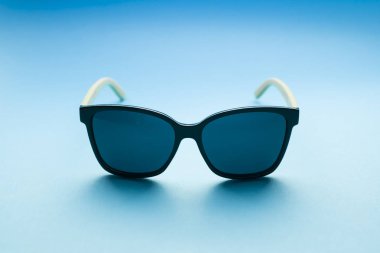 Pastel mavi arka plan üzerinde şık siyah güneş gözlüğü ön görünümü