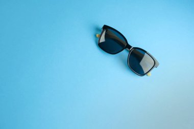 Pastel mavi arka plan üzerinde şık siyah güneş gözlüğü üst görünümü 