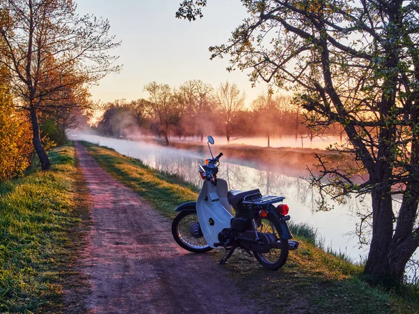 Mobilet, motosiklet gün doğumunda bir parkta toprak bir yolda.