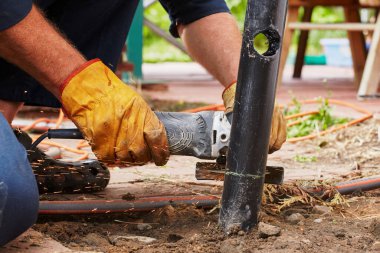 Açı öğütücü kullanan bir adam metal bir boru kesiyor.