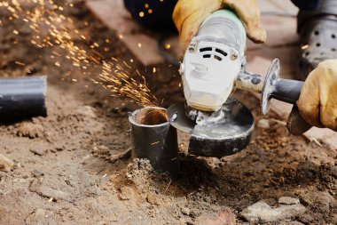 Açı öğütücü kullanan bir adam metal bir boru kesiyor.