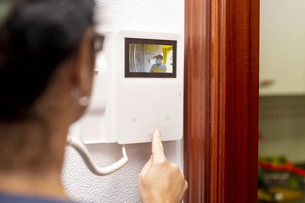 Kadın, dahili telefona dokunduktan sonra paket getiren kuryeye kapıyı açar