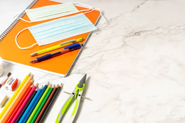 Okul malzemeleri, renkler, not defterleri ve koronavirüsün önlenmesi için malzemeler. Mermer arka planda. Salgın sırasında okula dönüş kavramı.