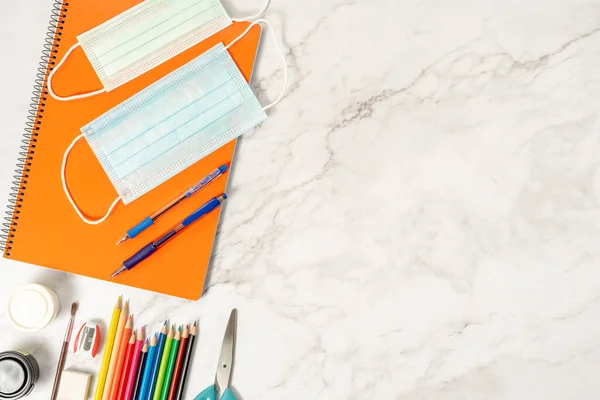 Okul malzemeleri, renkler, not defterleri ve koronavirüsün önlenmesi için malzemeler. Mermer arka planda. Salgın sırasında okula dönüş kavramı.