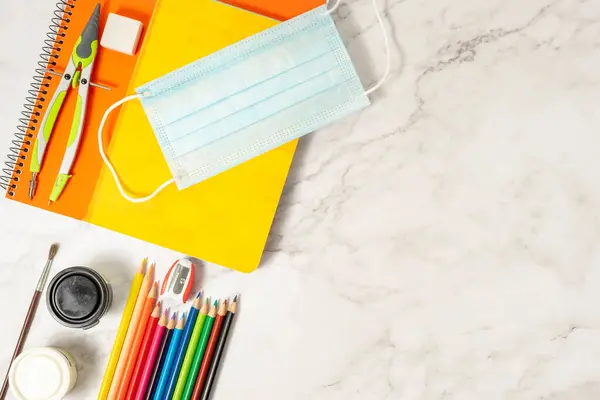 Okul malzemeleri, renkler, not defterleri ve koronavirüsün önlenmesi için malzemeler. Mermer arka planda. Salgın sırasında okula dönüş kavramı.