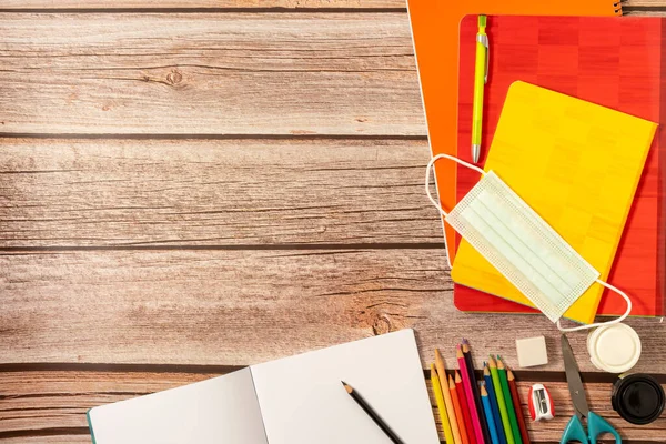 Okul malzemeleri, renkler, not defterleri ve koronavirüsün önlenmesi için malzemeler. Tahta bir üste. Salgın sırasında okula dönüş kavramı.