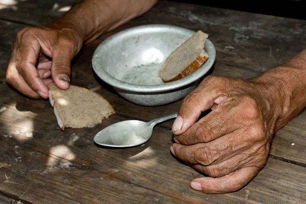 Zavallı yaşlı adamın kini, bir parça ekmeği nive boş kasesi ahşap zemine. Açlık ya da yoksulluk kavramı. Seçici odak. Emeklilikte yoksulluk. Evsiz. Sadaka