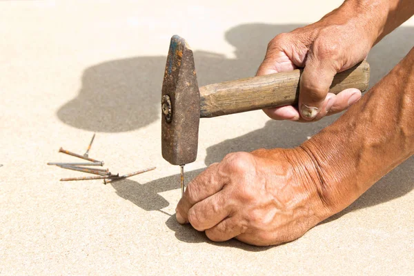 Yaşlı bir adamın elinde eski çekiç ve çivi. Marangoz hamm