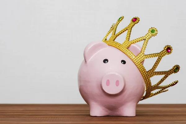金融の勝者または笑顔幸せピンク貯金箱木製テーブル 最高の将来の投資の黄金の冠を着てお金の節約のコンセプトの王 — ストック写真