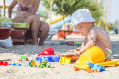 Sevimli bebek sahilde oyuncak oynuyor.