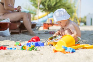 Sevimli bebek sahilde oyuncak oynuyor.