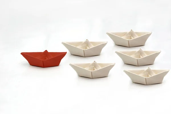 Leadership concept with red paper ship leading among white. Paper white ships swim behind the red