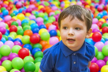 Gülümseyen bebek topları havuzda oynarken duygusal bir yüzü. Renkli topları ile oynayan mutlu çocuk. Bahçesi top bilardo renkli topları ile oynayan çocuk