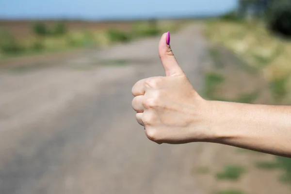 Thumb up is the symbol or sign of help or favor or hitchhike from hitchhiker on a road. Woman is showing her thumb for hitchhiking. White color skin hand showing the finger up symbol of hitchhiking, asking a car to stop