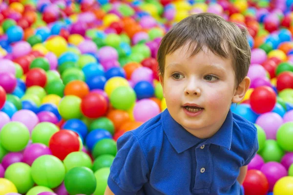 An emotional face of smiling baby playing in the balls pool. Happy kid playing with colored balls. Child playing with colorful balls in playground ball pool
