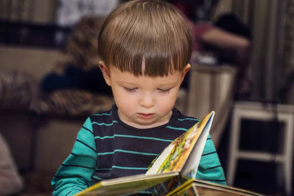 A little cute boy reading a book sitting on the floor. Child reading book at home