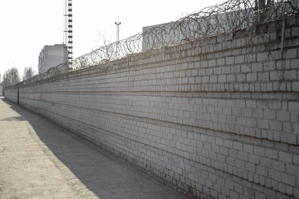 Brick fence with barbed wire above. The concept of prison or private property. Barbed wire on a brick wall. Barbed wired fence on the brick wall