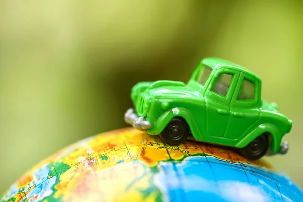 Toy car on the globe on green background. Miniature car toy on globe. Travel concept