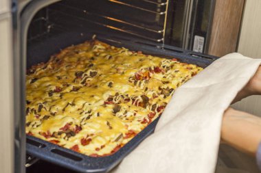 Ev yapımı biberli pizza fırında. Bir gaz fırında pişirme lezzetli pizza. Kadın taze pizza fırından alır.