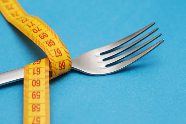 Measuring tape with fork on blue background. Concept of weight loss. Weight management. Healthy lifestyle. Weight loss health issue. Diet concept