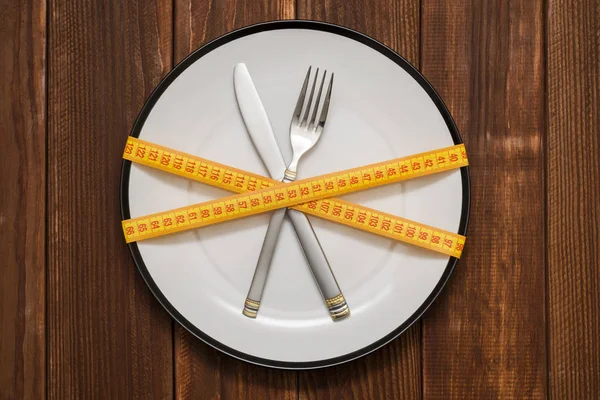 フォークとナイフは 測定テープでラップ ナイフとフォークでプレートは木製の背景に巻尺に包まれて 健康な食べることまたは概念をダイエットします ダイエットの概念 — ストック写真
