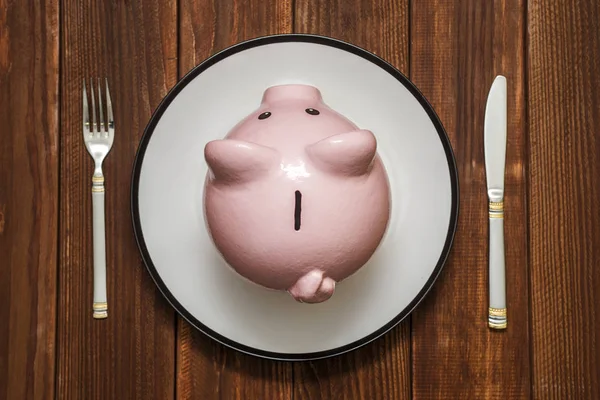 Pembe bir kumbara çanak üzerinde. Tasarruf tüketici kavramı. Kumbara tabak çatal ve bıçak. Mali kavramı