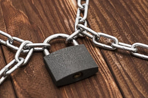 Padlock and chain on wooden background. Metal chain and locked padlock on wooden background