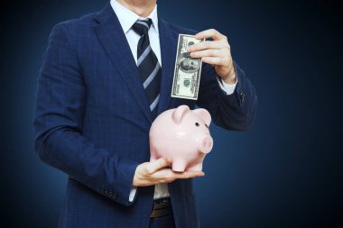 100 doları kumbara koyarak iş adamı. İş takım elbiseli adamı kumbara tutuyor. Finans tasarruf kavramı 