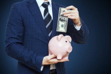 100 doları kumbara koyarak iş adamı. İş takım elbiseli adamı kumbara tutuyor. Finans tasarruf kavramı 