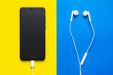 Mavi ve sarı arka plan üst görünümünde boş ekran ve kulaklık ile Akıllı telefon. Renkli arka planda kulaklıklar ve aygıtlar. Renkli arka planda kulaklıklı akıllı telefon