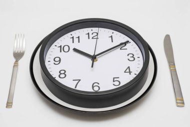 Bir çatal ve bıçak beyaz arka plan üzerinde saat yemek tabağı. Plaka ve bıçak üzerinde saat ve beyaz zemin üzerine çatal. Öğle yemeği saat kavramı