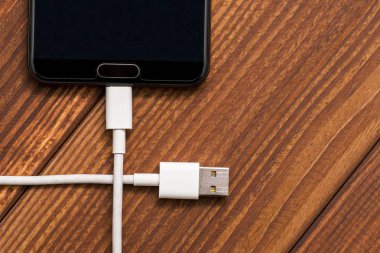 Ahşap masa üzerinde Usb kablosuyla smartphone. Akıllı telefon veya tablet hazır veri aktarımı veya pil şarj için Usb kablosu ile