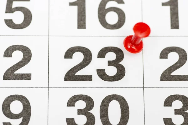 Pin on the date number 23. The twenty-third day of the month is marked with a red thumbtack. Pin on calendar. Calendar concept for important date, busy day, appointment or meeting reminder