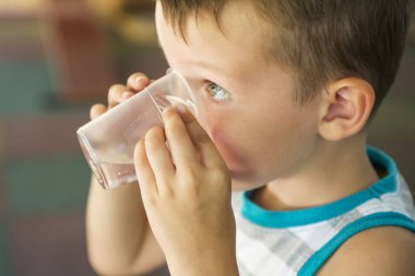 Çocuk elinde plastik bir bardak su tutuyor. Çocuk su içer. Sevimli küçük çocuk plastik bardaktatlı su içme