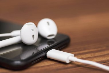 Ahşap arka planda kulaklıklı akıllı telefon. Ahşap arka planda beyaz kulaklıklar ve cep telefonu
