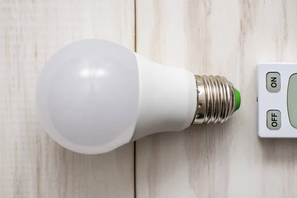 LED light bulb and remote control with buttons on and off on a white wooden background