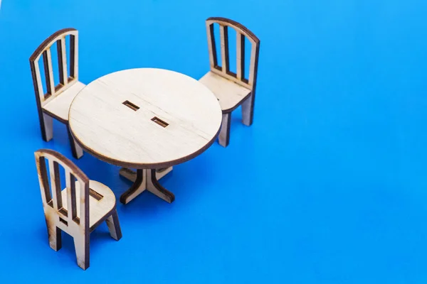 Miniature rustic wooden furniture on blue background. Vintage table and chairs with copy space