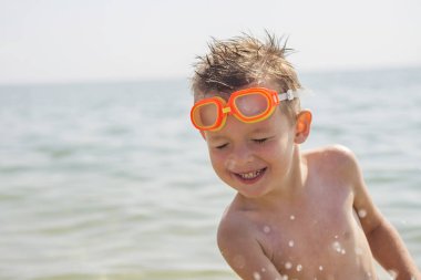 Denizde oynayan mutlu çocuk. Mutlu çocuk denizde yüzen deniz spreyinden gözlerini sıktı. Yaz tatili ve aktif yaşam tarzı konsepti